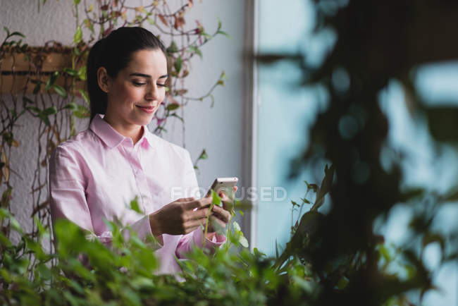 Portrait of businesswoman chatting with smartphone  near window in office. — Stock Photo
