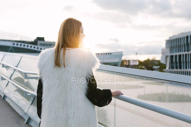 Rückansicht einer blonden Frau, die im Sonnenuntergang am Geländer posiert — Stockfoto