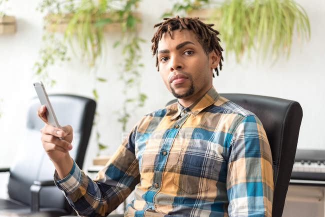 Mann mit Handy sitzt im Bürostuhl und blickt in Kamera — Stockfoto
