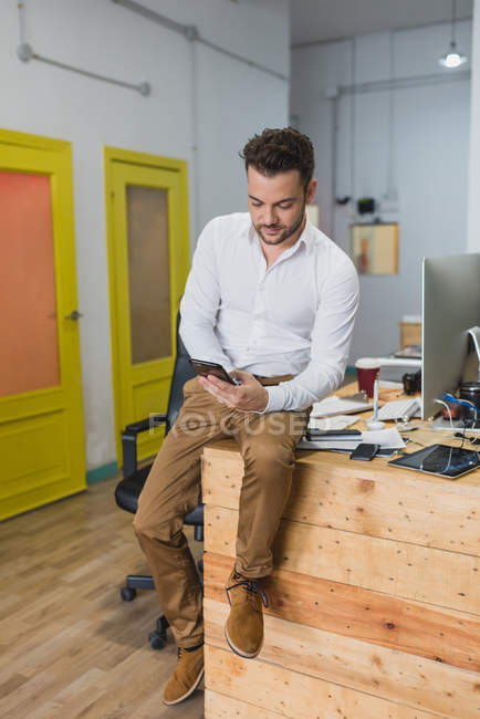Portrait of man sitting at table in office and browsing phone. — Stock Photo