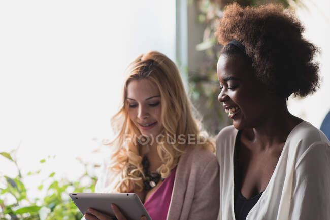 Portrait of two women standing near window and browsing tablet — Stock Photo