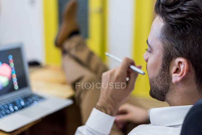 Uomo che tiene la penna e guardando il computer portatile con attenzione
. — Foto stock