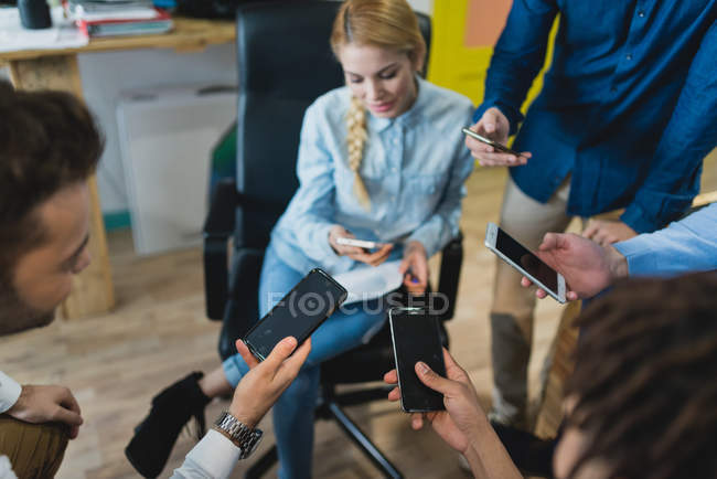 Visão de alto ângulo de trabalhadores de escritório olhando para smartphones enquanto reunião diária no escritório — Fotografia de Stock