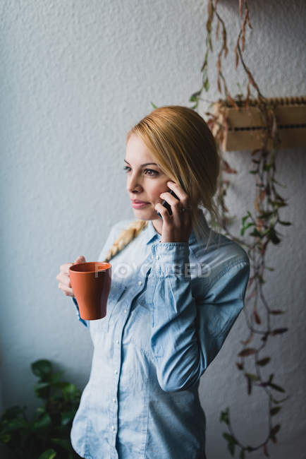 Ritratto di giovane donna bionda con in mano una tazza e telefono parlante — Foto stock