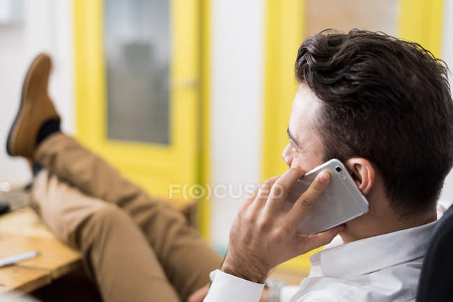 Side view of man put legs on table and having a phone conversation. — Stock Photo