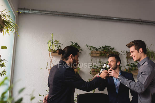 Вид збоку щасливих людей, які клацають пляшки пива в офісі після робочого часу — стокове фото