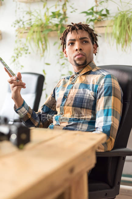Mann sitzt mit Smartphone am Büroarbeitsplatz und schaut zur Seite — Stockfoto