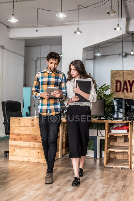 Zwei Büromenschen, die im Büro spazieren gehen und Tablets durchsuchen — Stockfoto