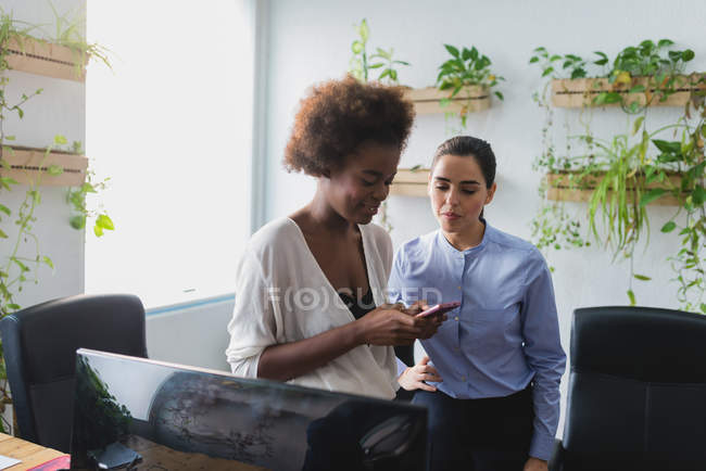 Porträt einer Geschäftsfrau, die im Büro auf den Smartphone-Bildschirm ihrer Kollegen blickt — Stockfoto