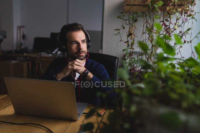 Портрет людина в навушниках, сидячи за столом з ноутбуком і дивитися вбік — стокове фото