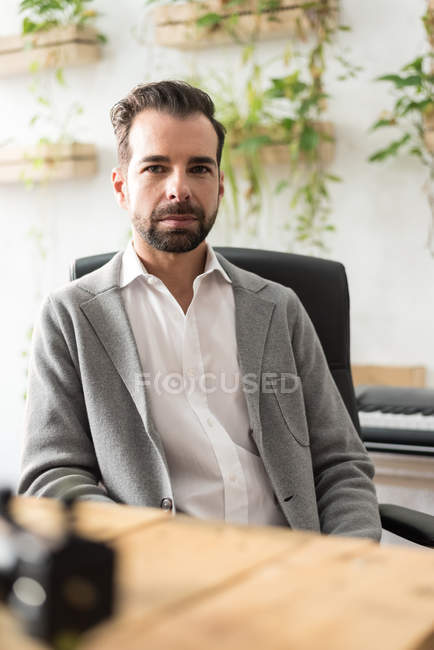 Confident bearded businessman sitting at workplace in office and looking at camera — Stock Photo
