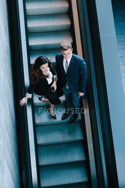 Do acima mencionado negócio Casal em movimento na escada rolante — Fotografia de Stock