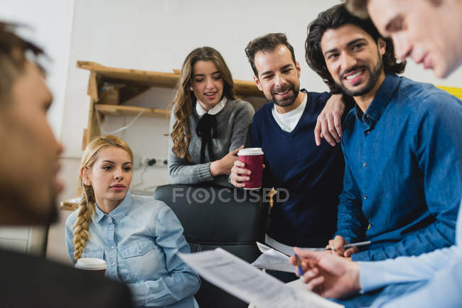 Retrato de los miembros sonrientes del equipo de la oficina escuchando el informe de sus colegas en la reunión diaria - foto de stock
