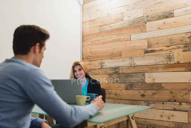 Вид ззаду чоловіка, який дивиться на жінку, друкуючи на ноутбуці в кімнаті для переговорів — стокове фото