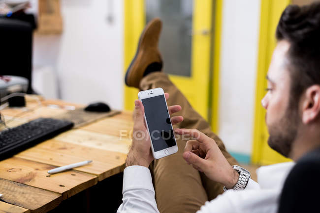 Businessman sitting in chair with legs on table and browsing smartphone — Stock Photo