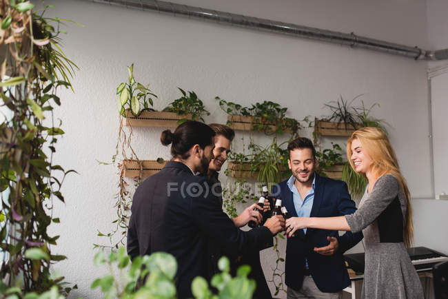 Felices compañeros de trabajo golpeando botellas de cerveza en la oficina después del tiempo de trabajo - foto de stock