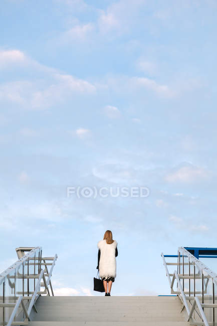 Visão traseira da mulher elegante posando no topo das escadas urbanas sobre o céu — Fotografia de Stock
