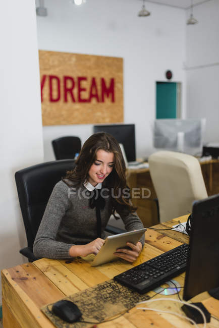 Portrait of woman sitting at  desk in open space office and browsing tablet. — Stock Photo