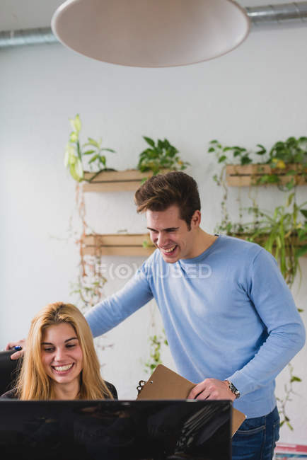 Portrait of smiling man and woman looking at screen of computer in office. — Stock Photo