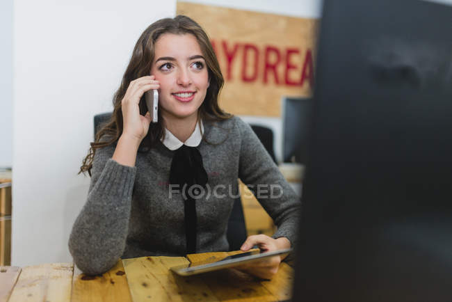Portrait of young lady having phone conversation and holding a tablet — Stock Photo