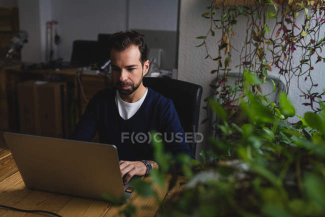 Retrato del hombre sentado en la mesa y el uso de la computadora portátil en el lugar de trabajo - foto de stock