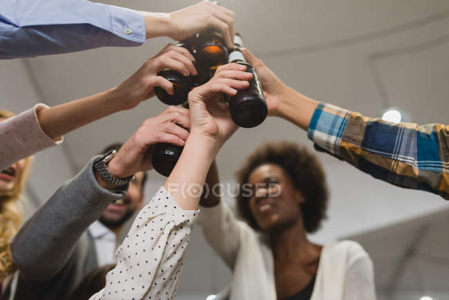 Низкий угол обзора коллег, стучащих бутылками в офисе во время построения команды — стоковое фото