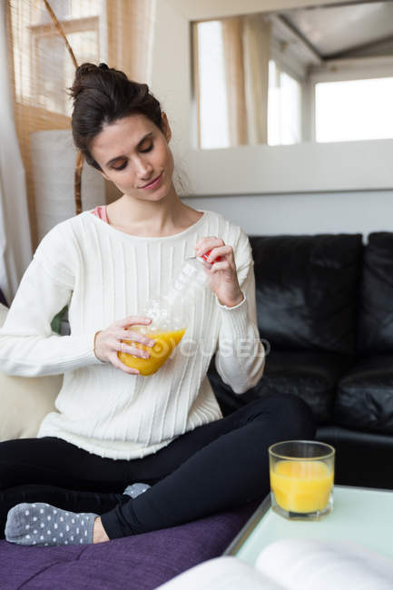Portrait of woman sitting on coach with legs and closing bottle of orange juice — Stock Photo