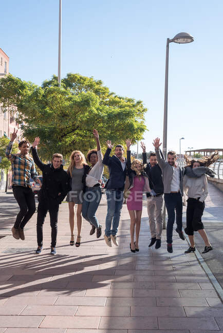 The people placed in one line jumping in the street at the same time. Vertical outdoors shot. — Stock Photo