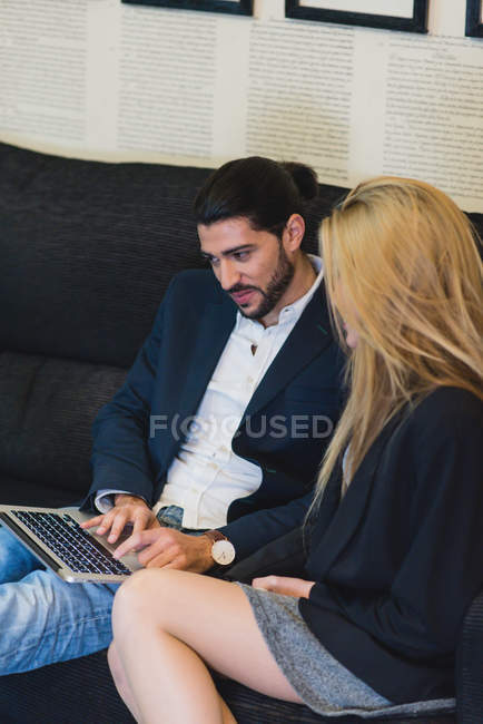 Portrait of colleagues sitting at couch in office and browsing laptop. — Stock Photo