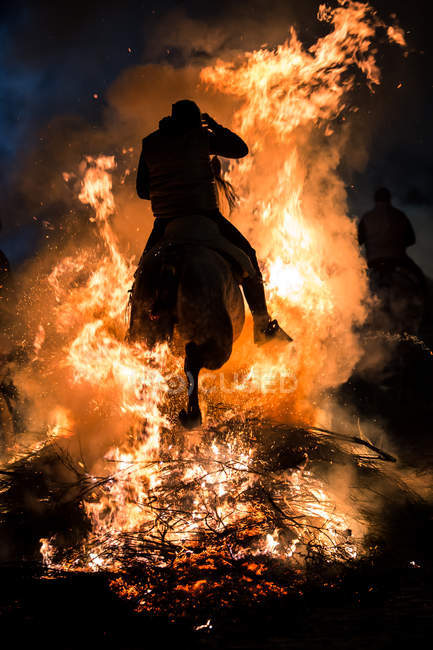 Vue arrière de l'équitation à travers le feu de joie dans le rituel de purification la nuit — Photo de stock