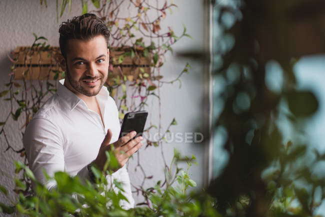 Portrait of businessman browsing smartphone and looking at camera near window in office. — Stock Photo