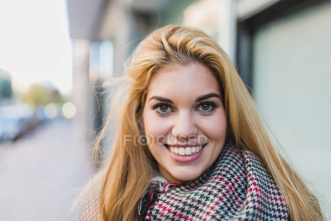 Portrait of smiling blonde woman looking at camera at street scene — Stock Photo