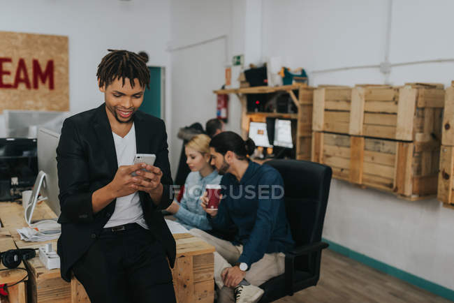 Portrait of smiling businessman sitting at table and using smartphone in office — Stock Photo