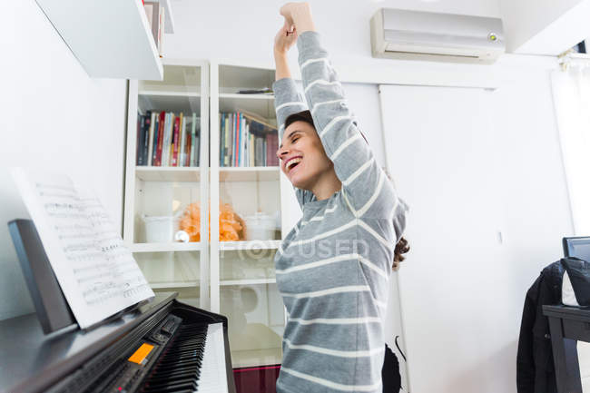 Side view of brunette girl sitting at piano and cheerfully stretching hands up — Stock Photo