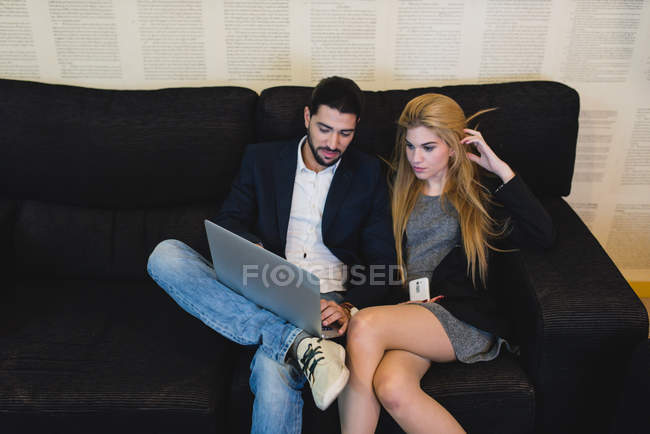 Portrait of colleagues sitting at couch in office and browsing laptop. — Stock Photo
