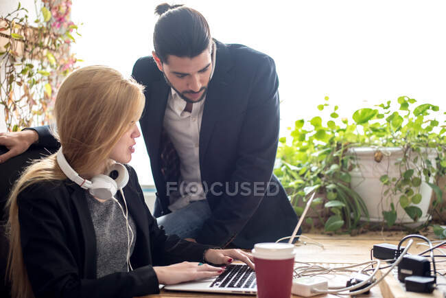 Hombre sentado en la mesa y comunicándose con la mujer que trabaja con el ordenador portátil. Horizontal en interiores tiro. - foto de stock