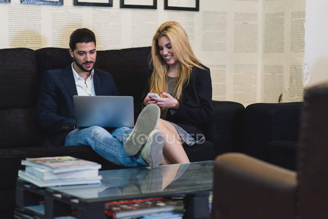 Ritratto di colleghi seduti sul divano in ufficio e computer portatile di navigazione . — Foto stock