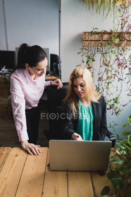 Портрет улыбающихся женщин, просматривающих ноутбук в офисе — стоковое фото