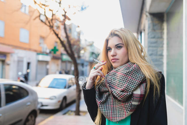 Portrait of blonde girl smoking a cigarette near office — Stock Photo