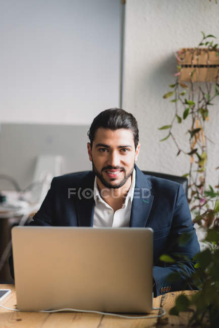 Ritratto di uomo d'affari seduto sul posto di lavoro e guardando la fotocamera sul computer portatile — Foto stock