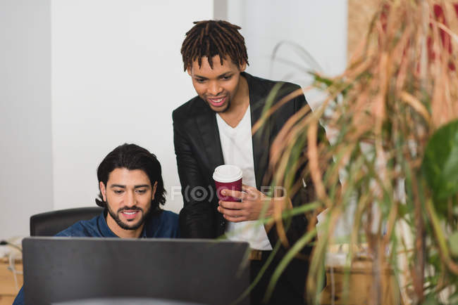 Портрет улыбающегося бизнесмена с кофе, смотрящего на экран компьютера коллег — стоковое фото