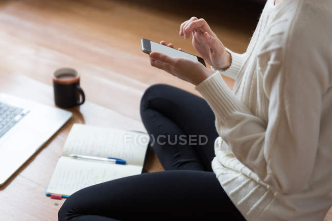 Обрізати зображення жінка сидить на підлозі і перегляду смартфон. — стокове фото
