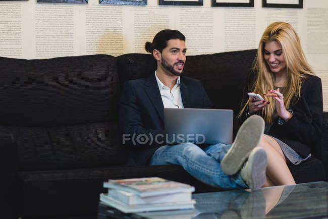 Portrait of colleagues sitting at couch in office and browsing devices — Stock Photo