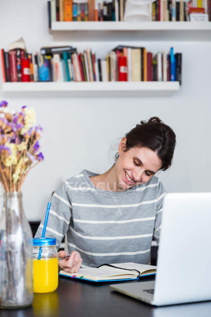 Donna sorridente seduta al computer portatile e guardando giù al notebook — Foto stock