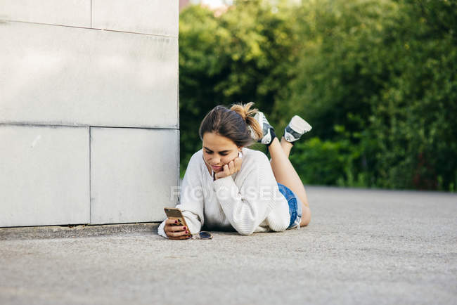 Chica de navegación teléfono mientras está acostado en el suelo - foto de stock
