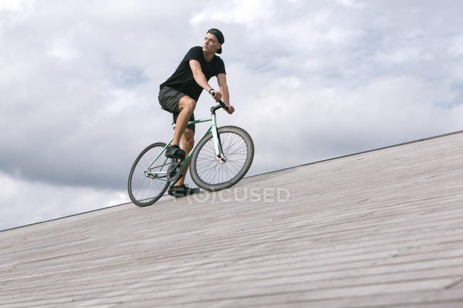 Задумчивый молодой человек в кепке на велосипеде — стоковое фото