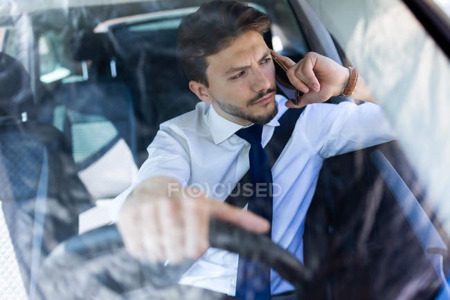 Jeune homme en costume parler au téléphone tout en conduisant voiture — Photo de stock
