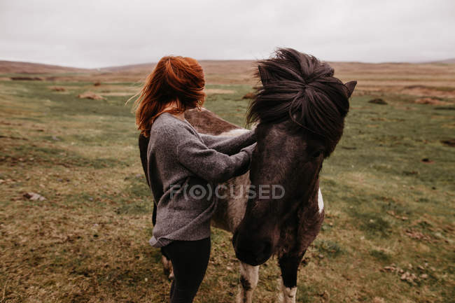 Mujer acariciando caballo en el pasto - foto de stock