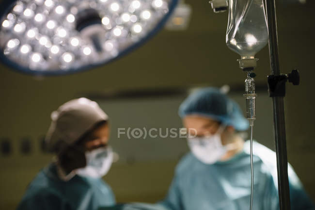 Tropfflasche über verschwommenen Chirurgen — Stockfoto