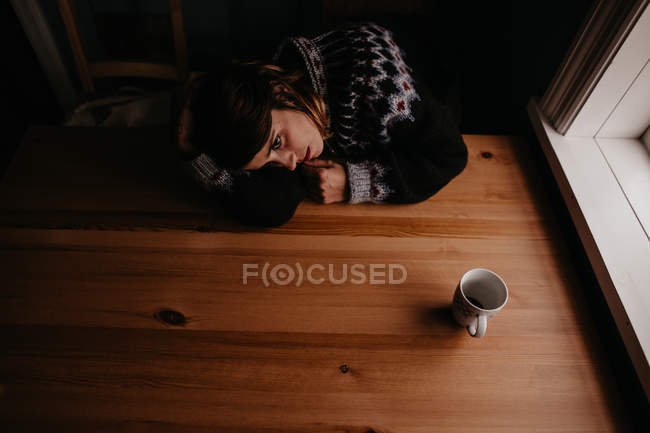 Mulher deitada na mesa com caneca — Fotografia de Stock